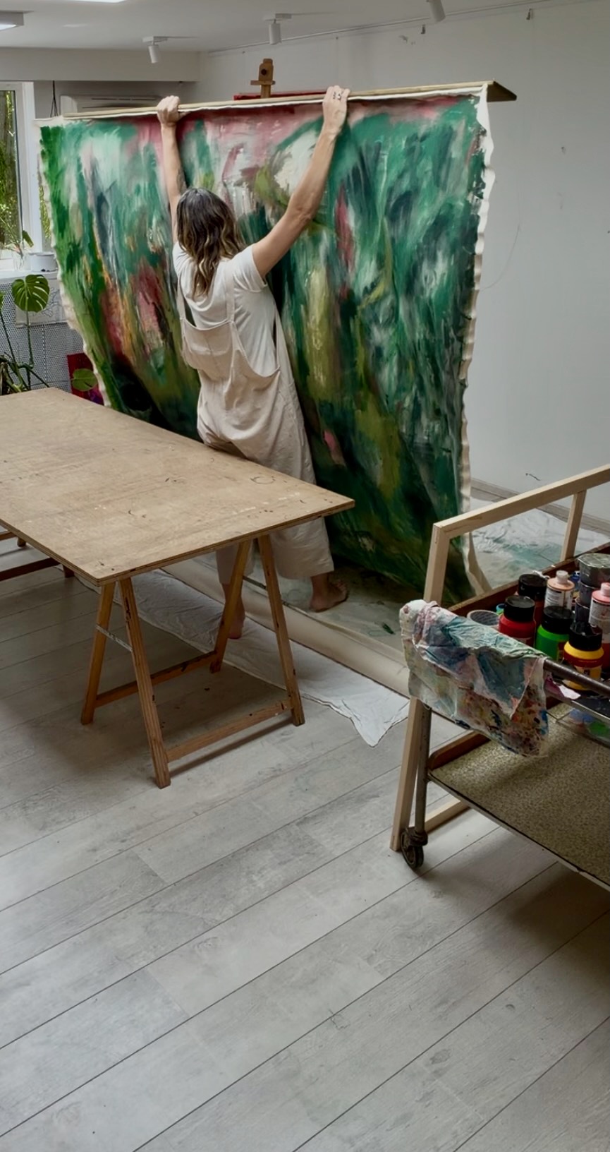 Nicky Myny lifting a large green painting in her Belgian studio, arms raised