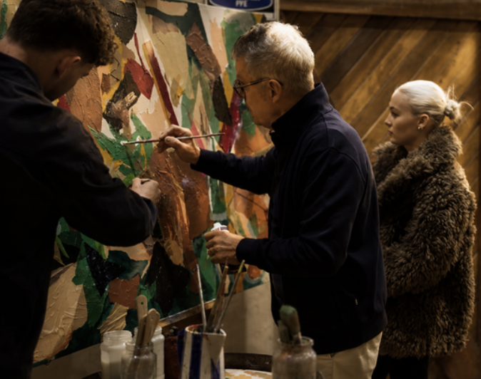 Three people painting together on a shared canvas at Harvest Fest